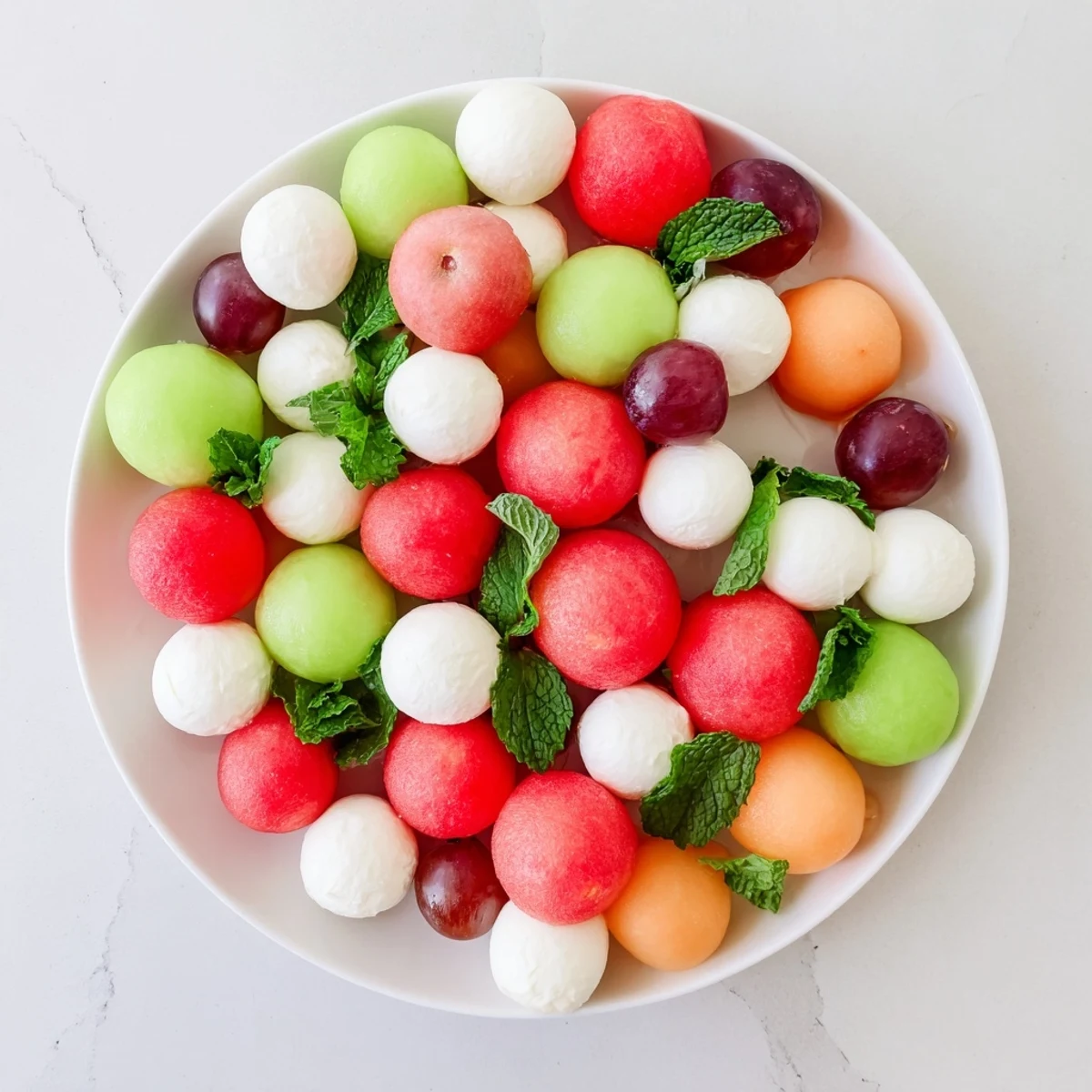 A colorful and fresh polka dot platter appetizer with melon, cheese balls, and grapes ready to serve.