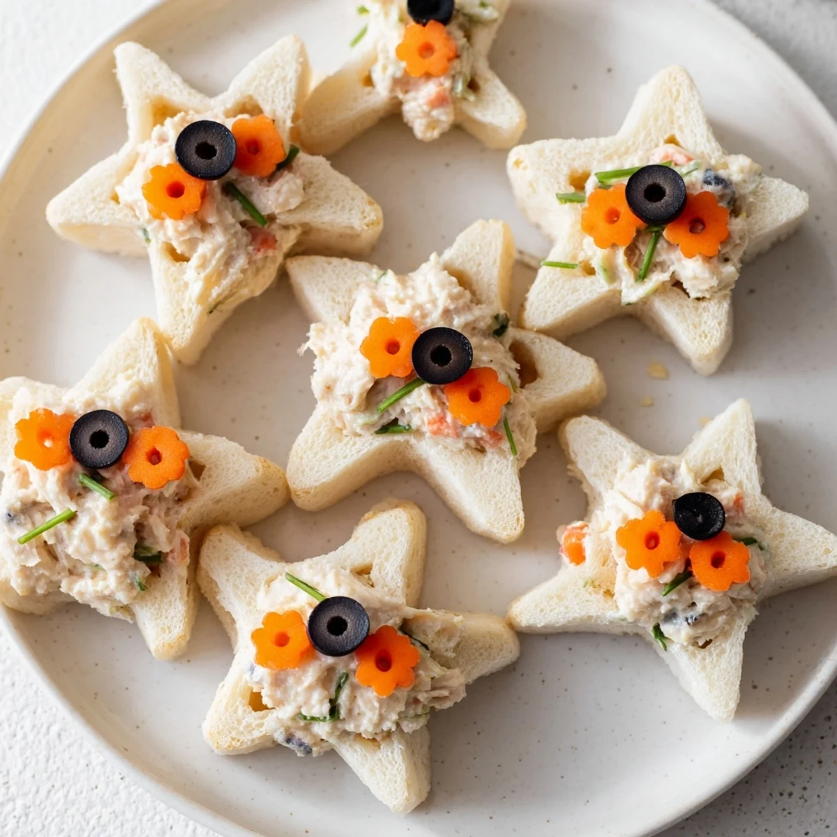 Golden star-shaped Mini Starfish Sandwiches, filled with tuna salad and olive eyes, ready to eat.