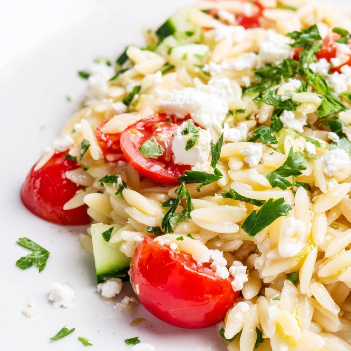 A serving spoon dips into a chilled bowl of Greek Orzo Salad, showcasing the zesty lemon-oregano dressing and tender pasta.