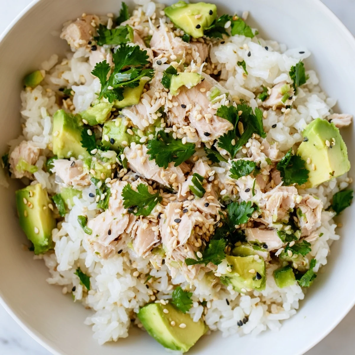 Forkful of Tuna Avocado Rice Bowl with toasted sesame seeds and fresh cilantro, served in a white ceramic bowl.