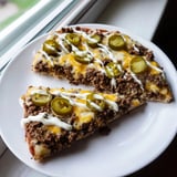 A close-up of a bubbling, cheesy ground beef taco pizza topped with fresh, green onions.