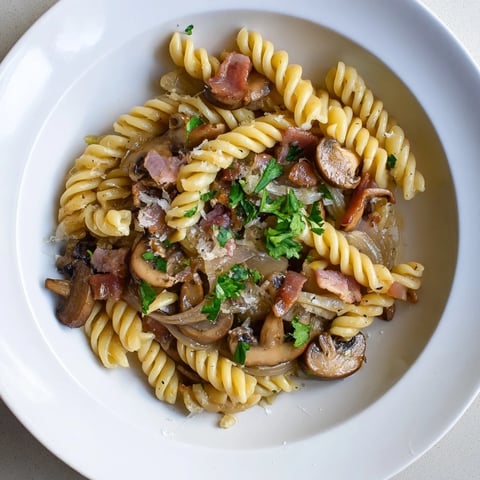 A fork twirls fusilli with bacon, onions, and mushrooms, a comforting Italian-inspired pasta meal.