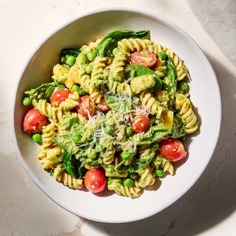 Steaming bowl of One-Pot Creamy Pesto Pea Protein Pasta, with vibrant green peas and tomatoes.
