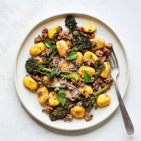 Golden-brown Sheet Pan Gnocchi Bake with crispy Italian sausage and tender broccolini, garnished with Parmesan.