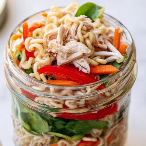 Bright mason jar meal prep with noodles, tofu, and bell peppers in a savory sauce beside lime wedges.
