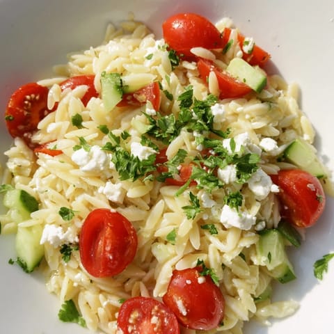 Overhead view of a vibrant Greek Orzo Salad tossed with red onion, Kalamata olives, and fresh herbs on a wooden table.