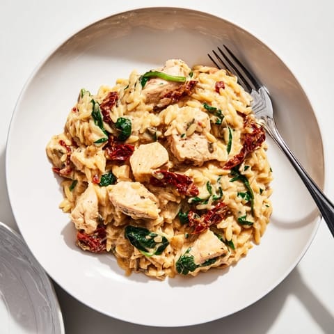 Creamy Tuscan Chicken Orzo served in a skillet, garnished with fresh basil and a sprinkle of Parmesan cheese.