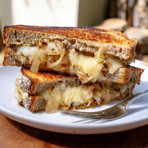 A close-up of a Caramelized Onion & Gruyère Grilled Cheese shows crispy, buttery bread and gooey, nutty cheese against a rustic background.