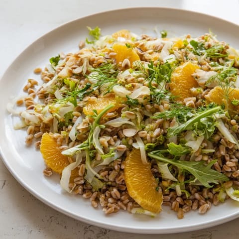 Served in a white ceramic bowl, this Farro Salad With Fennel, Oranges, and Almonds is topped with vibrant orange zest and fennel fronds, a light lunch or refreshing side dish.