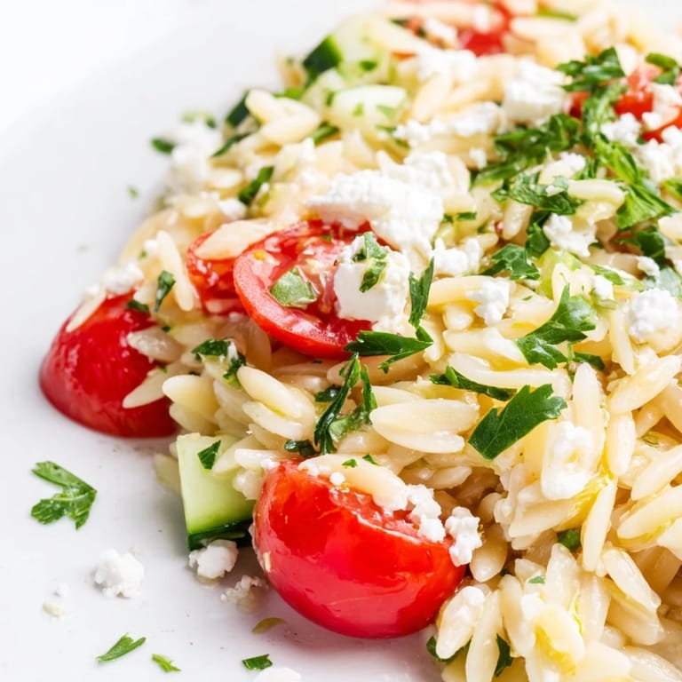 A serving spoon dips into a chilled bowl of Greek Orzo Salad, showcasing the zesty lemon-oregano dressing and tender pasta.